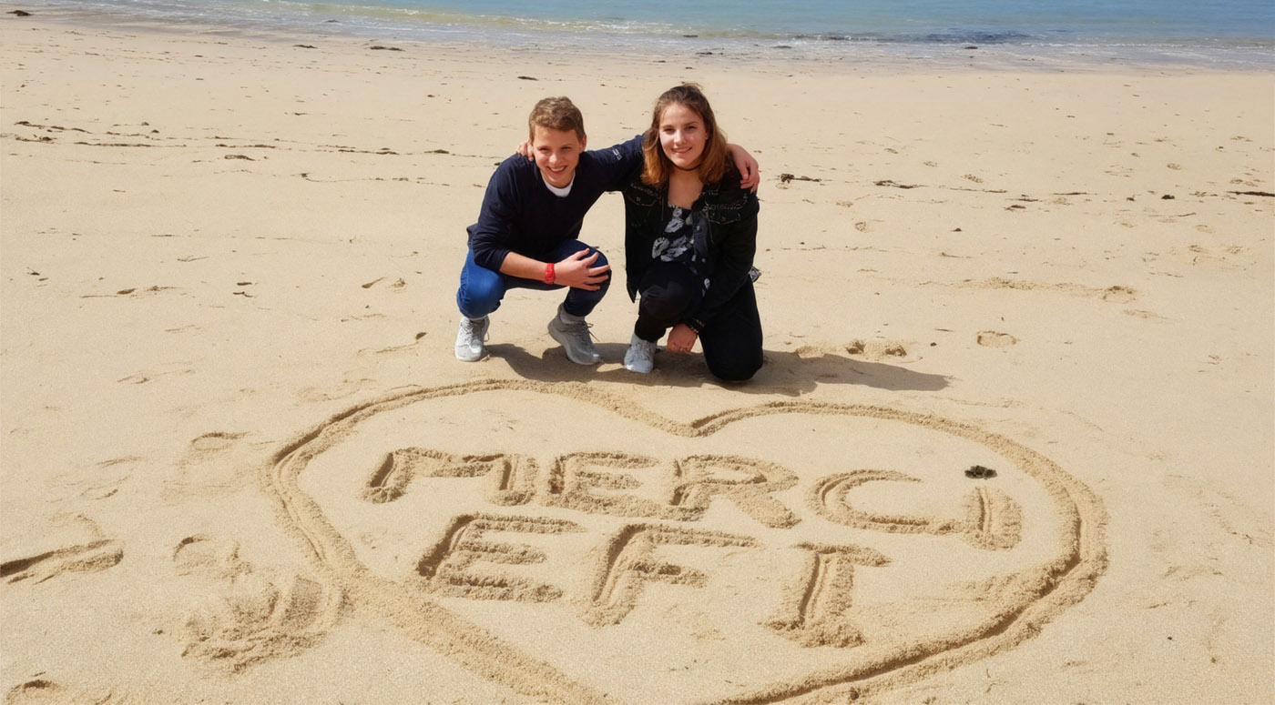 A couple kneeling on a sandy beach with 'MERCI EFT' written in the sand.